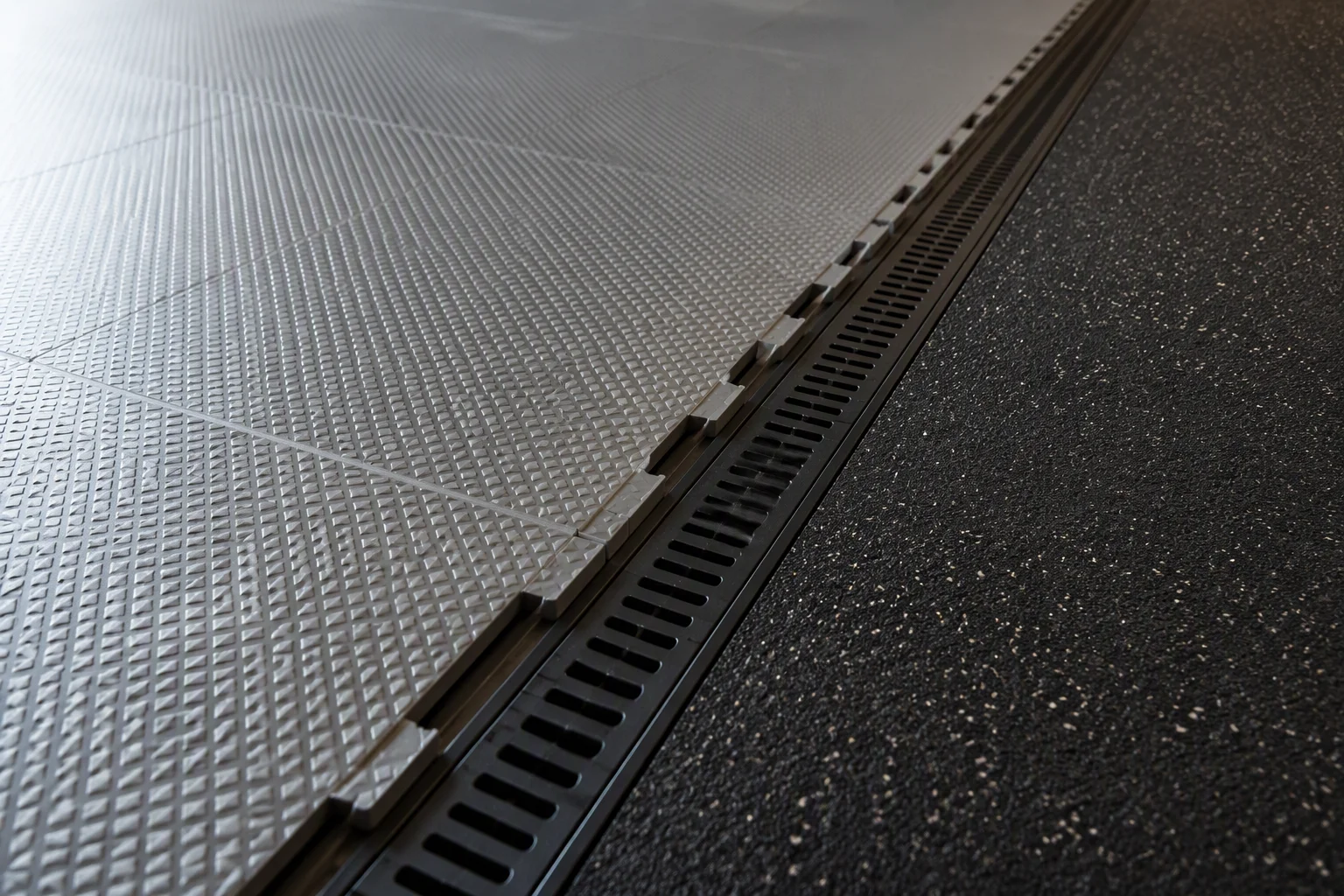 Interlocking garage floor tiles transitioning to a rubber zone with an integrated drainage channel