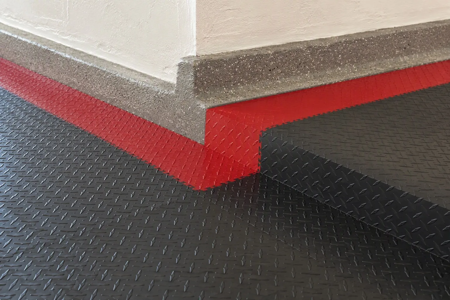 Charcoal garage floor tiles with red accent border row and precisely cut tile edge against the wall