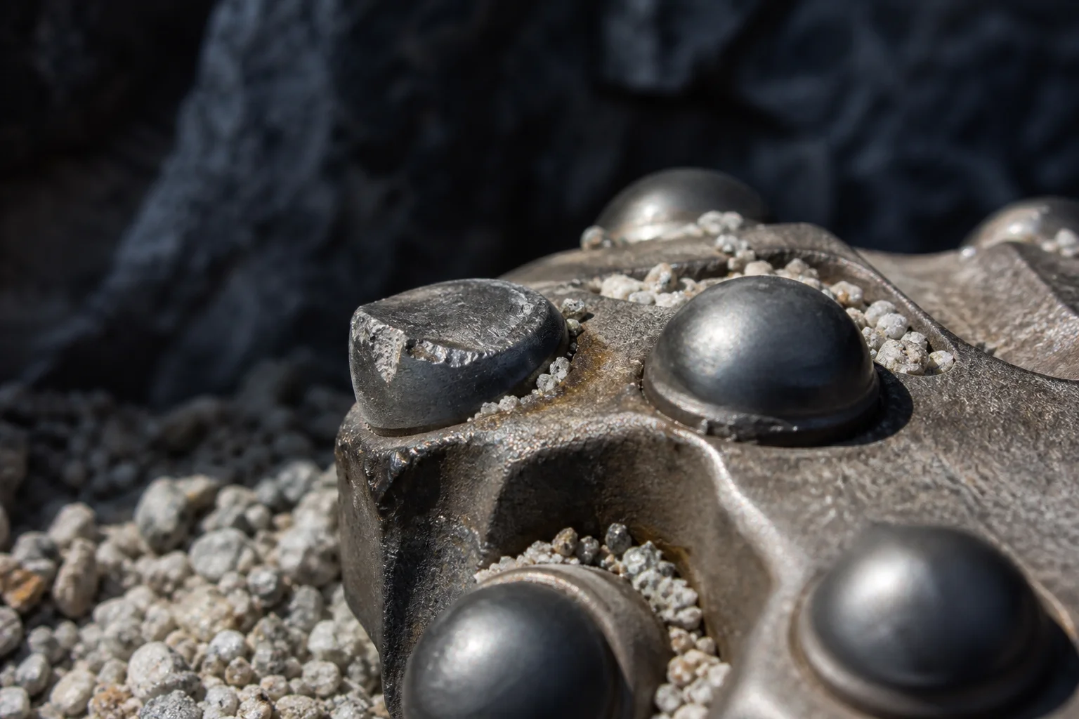 Macro view of a flattened and chipped carbide button on a rock drill bit beside an intact button