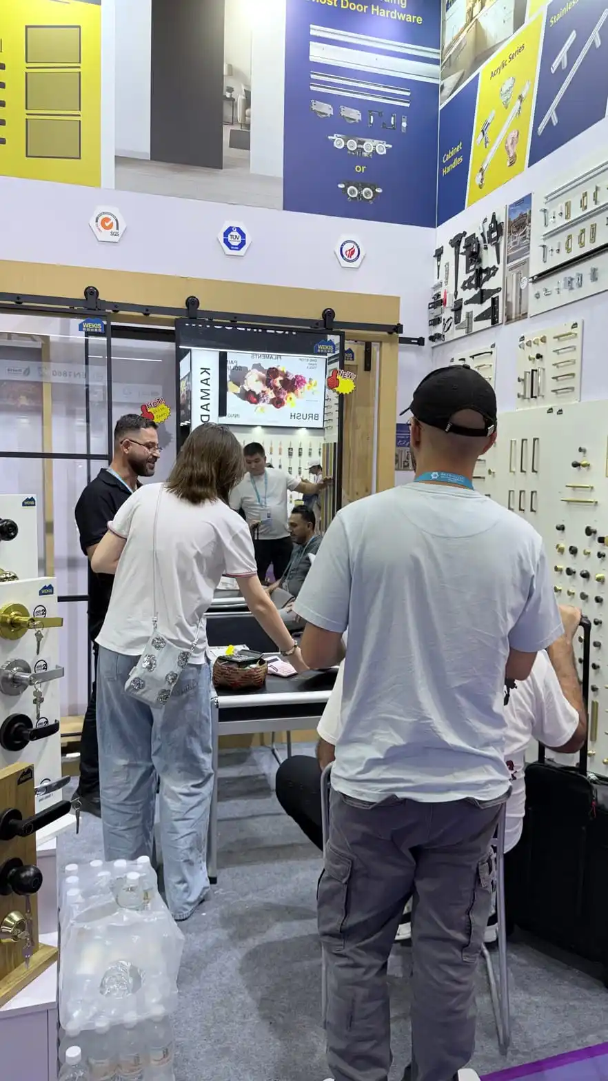 Un acheteur examine les différentes finitions possibles pour les poignées de meubles sur le stand Wekis.