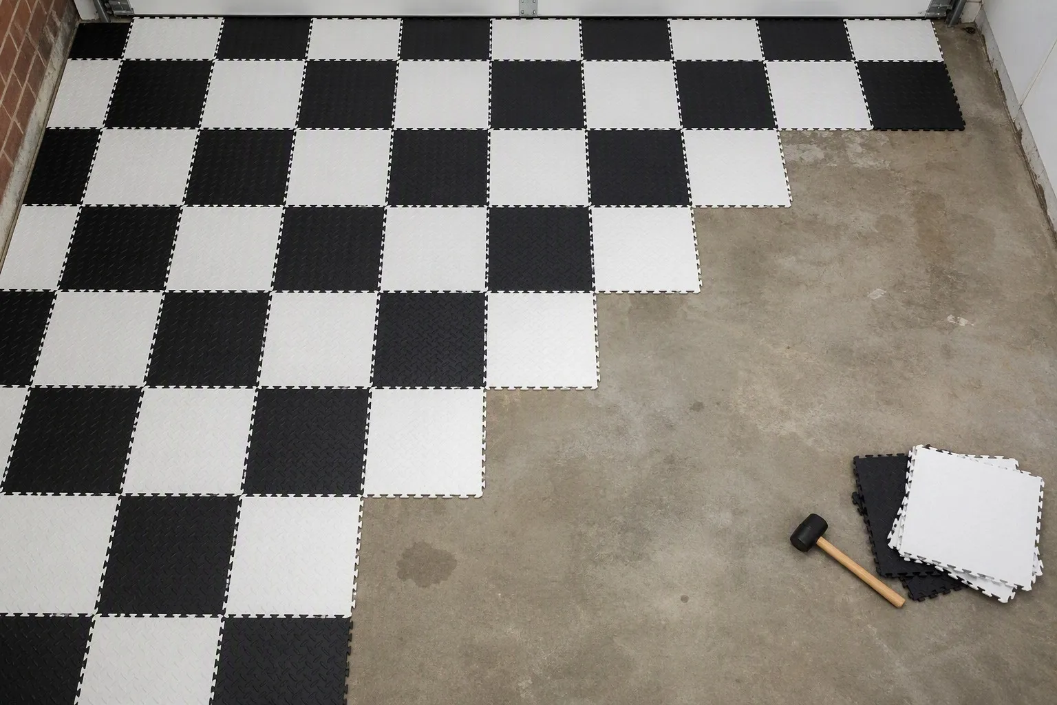 Installing black and white checkerboard pattern with interlocking garage floor tiles halfway across the floor