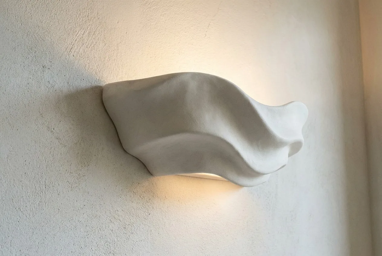 Sculptural plaster wall lamp with organic wave textures on a limewash wall