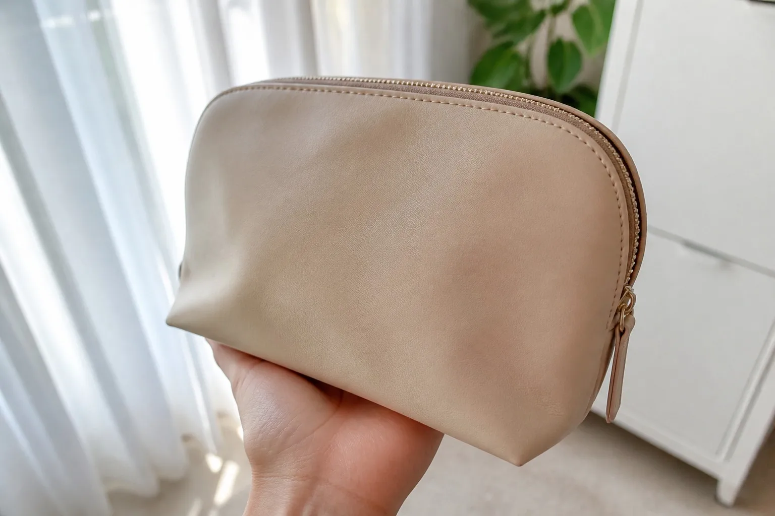 Hand holding a single unbranded cream PU leather cosmetic bag sample in natural daylight
