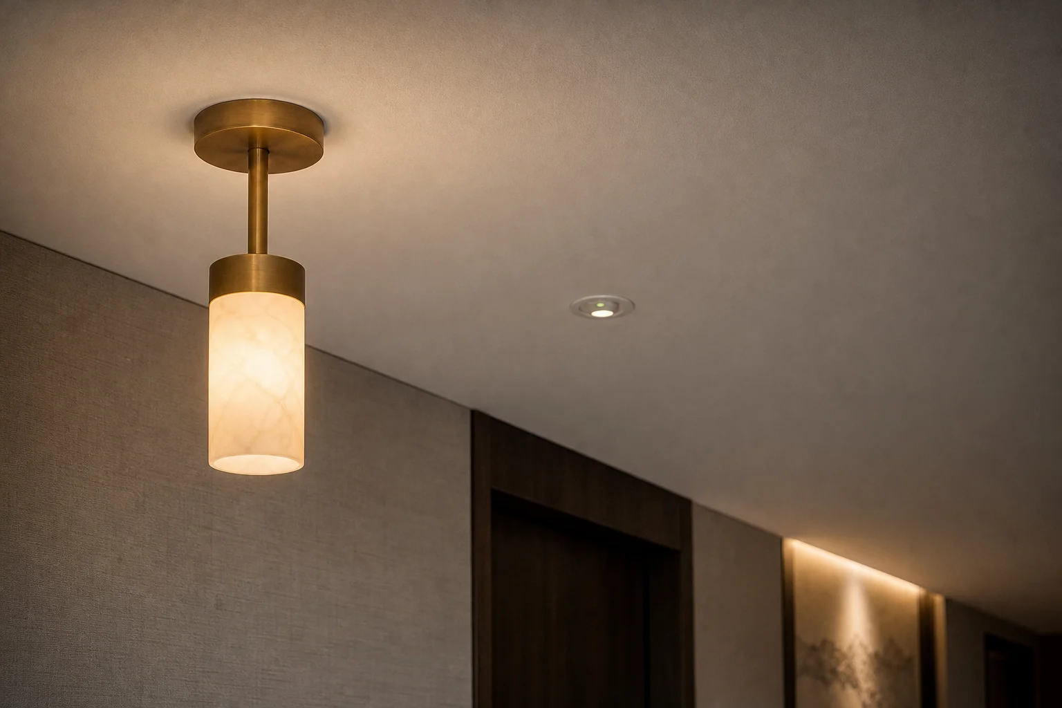 Decorative pendant and recessed emergency downlight on one hotel corridor ceiling