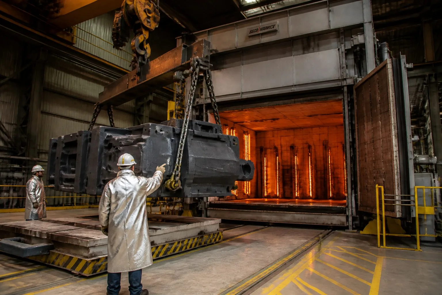 Workers loading large steel castings into industrial heat treatment furnace