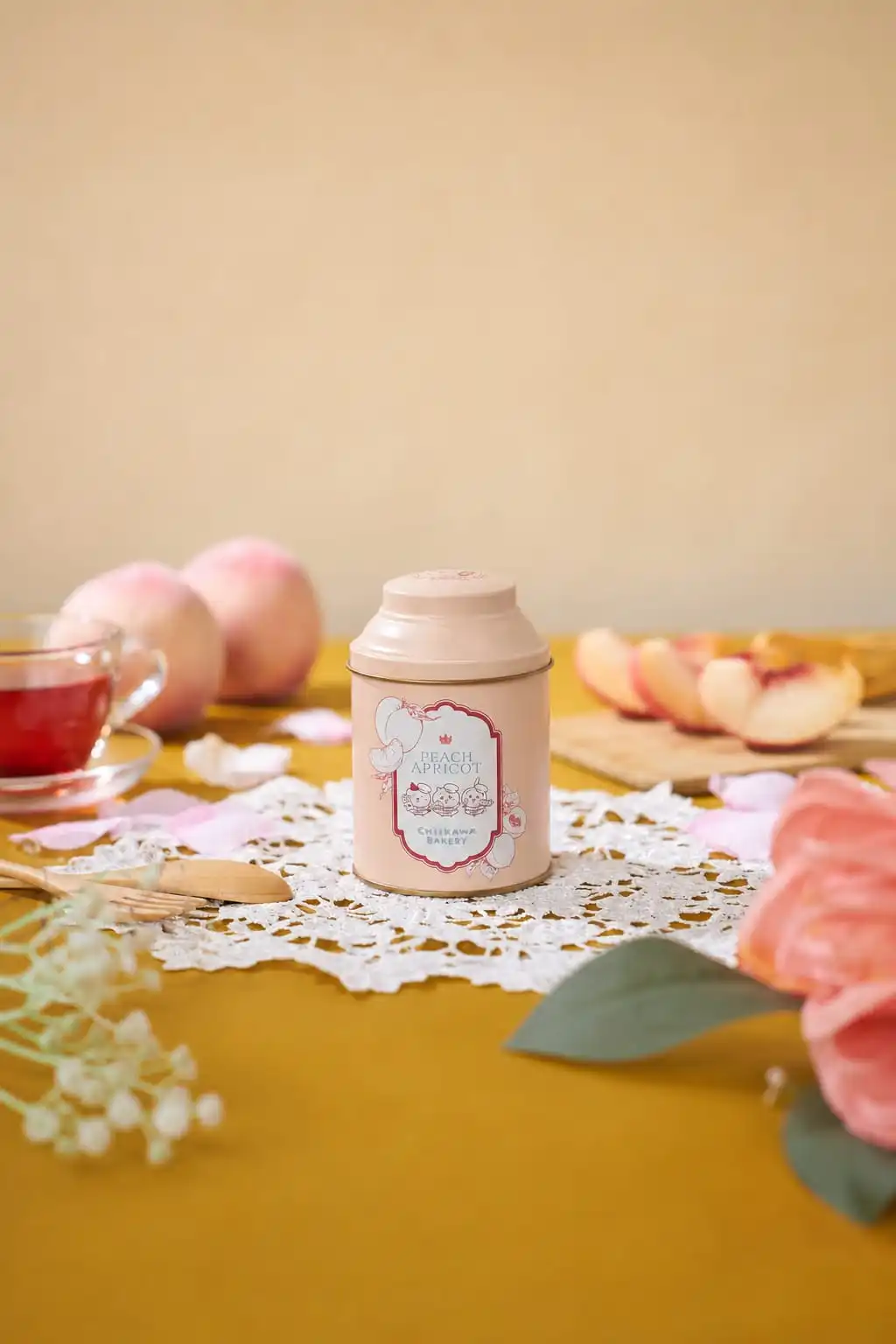 Chiikawa Bakery Peach Apricot tea tin on a lace mat with peaches, apricots and a glass of tea