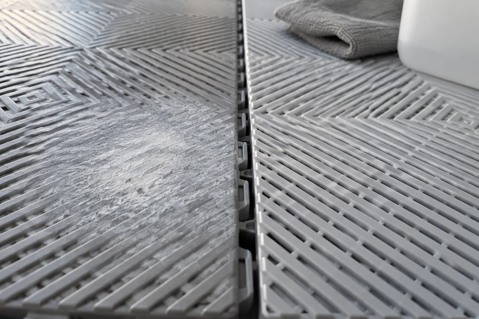 Close-up of a garage floor tile with a chalky faded patch beside a clean interlocking tile