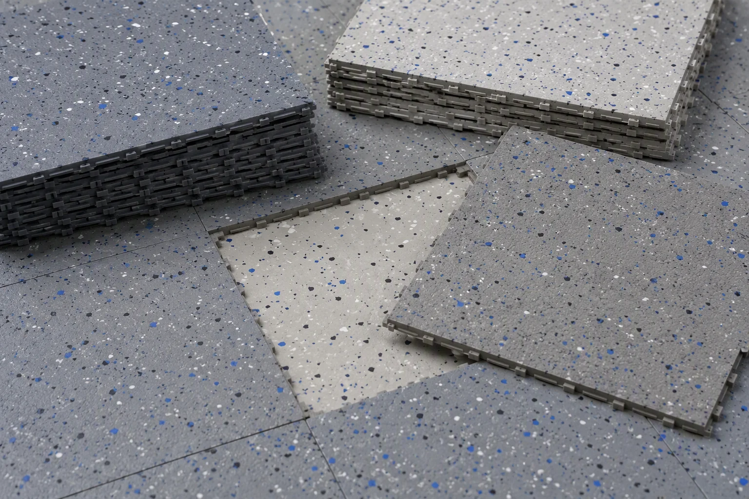Sun-faded garage floor tile panels stacked beside new matching interlocking tiles