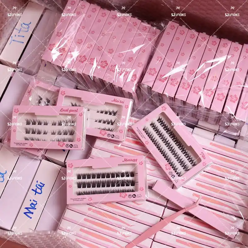 Bulk production of pink hibiscus lash sleeves and cards in plastic bags, with open cards showing lash clusters, style names and vegan and handmade badges - card and sleeve lash packaging production