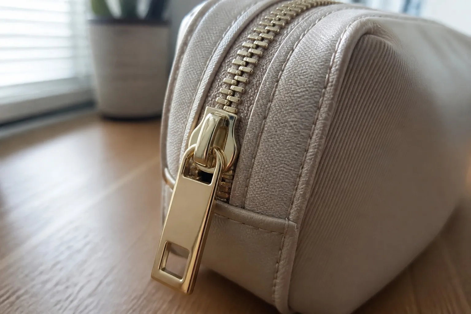 Close-up of a gold metal zipper puller and stitched edge on a custom cosmetic bag