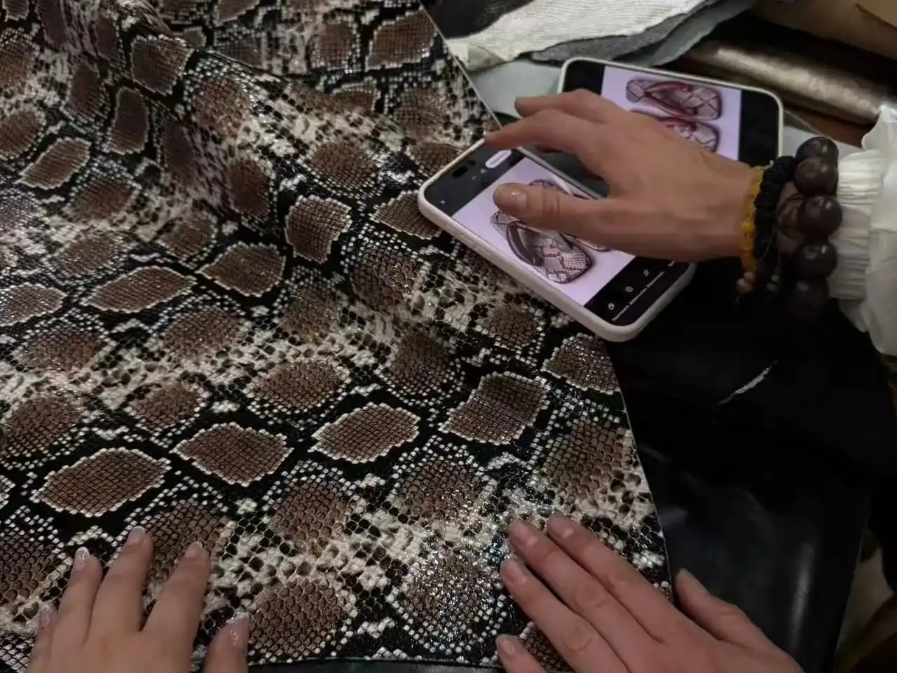 Hands spreading a large python-print leather hide and comparing it against a design on a phone