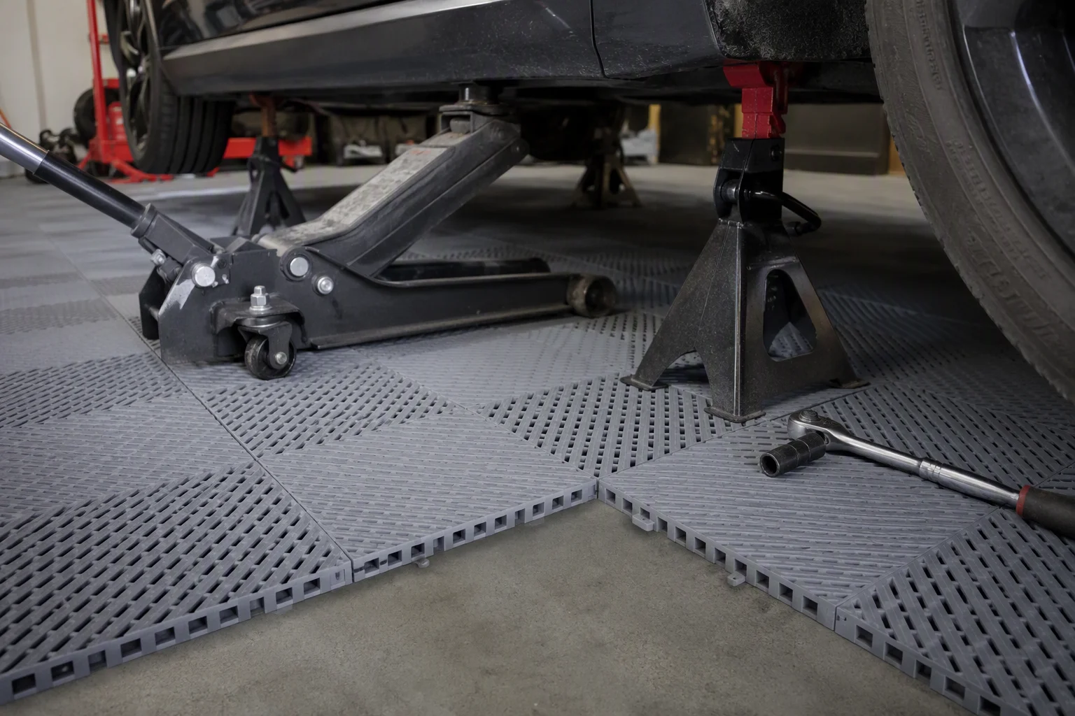 Floor jack and jack stands supporting a car on garage floor tiles