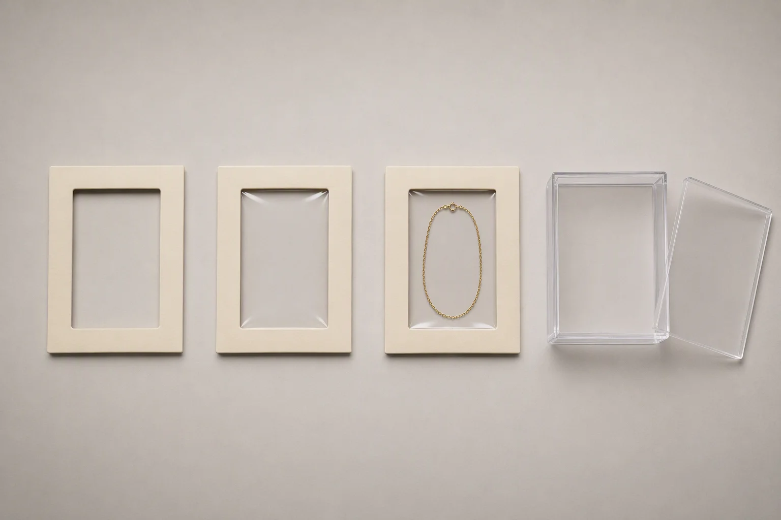 Overhead flat-lay on a pale warm-grey surface showing four clear and membrane jewelry box components in a horizontal row: at left a cream board frame with a cut rectangular aperture and no film, next to it the same frame with taut transparent film stretched across the aperture, then the same frame with film over a fine gold chain lying flat behind it so the chain reads as suspended, and at right a rigid box built from clear transparent sheet with its flat clear lid resting slightly offset beside it