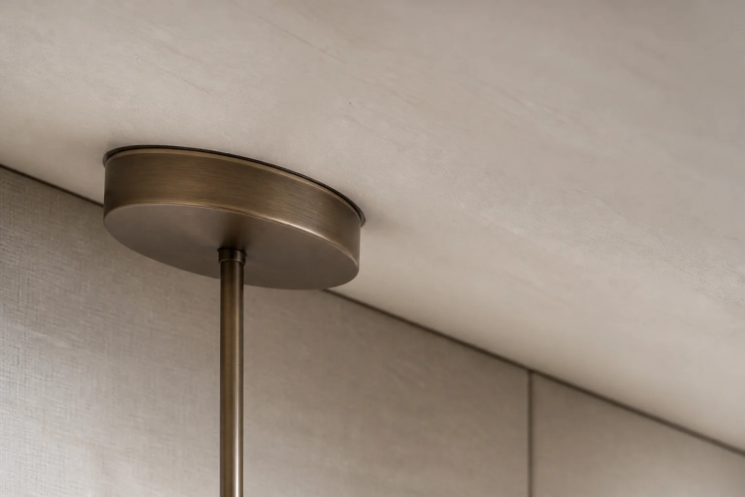 Brushed bronze pendant canopy sitting flush on a sloped plaster ceiling with a plumb stem