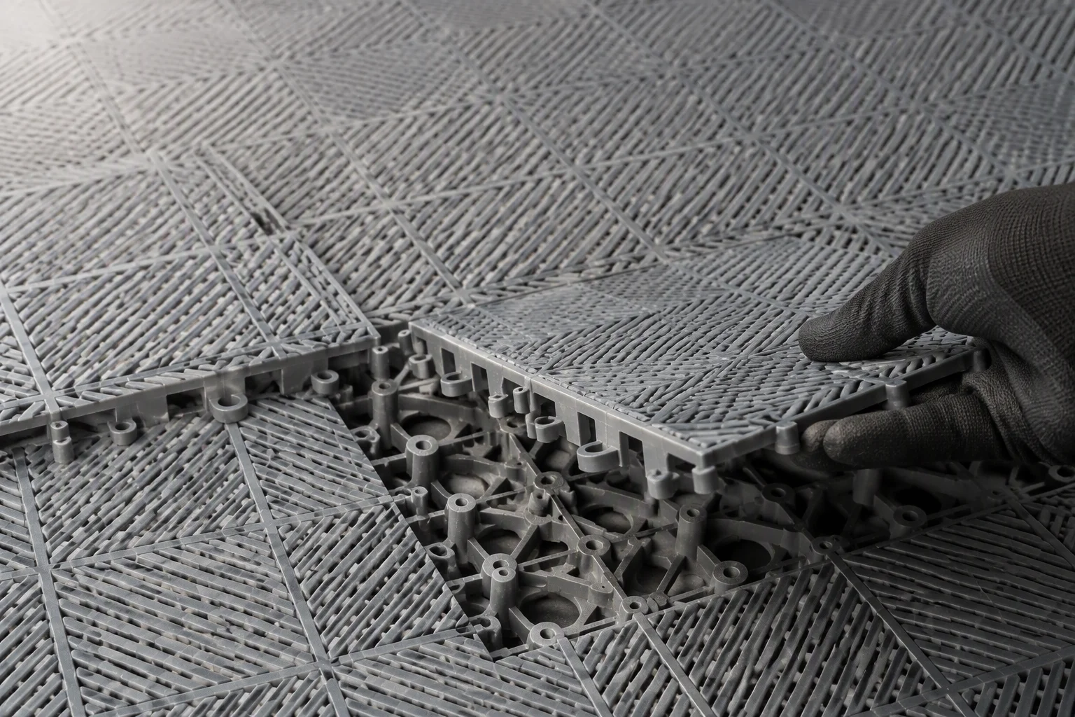 Lifting one interlocking floor tile to inspect the locking lugs under a damaged garage floor tile