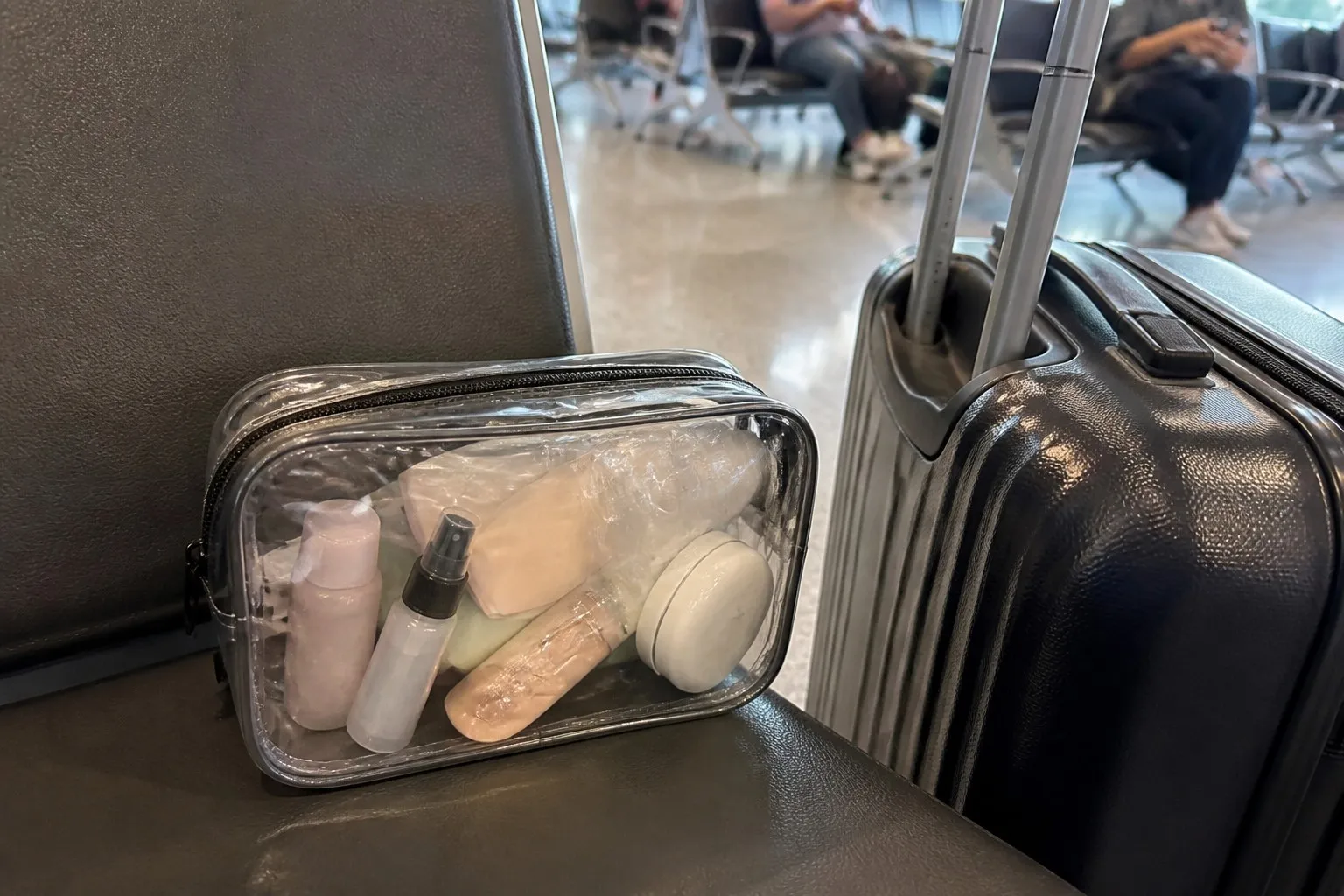 Clear transparent TPU cosmetic bag on an airport seat beside a carry-on suitcase