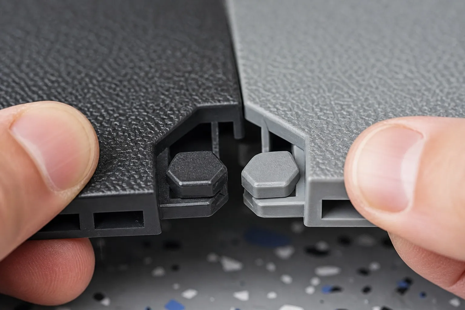 Hand connecting two interlocking garage floor tiles with hexagonal locking pins