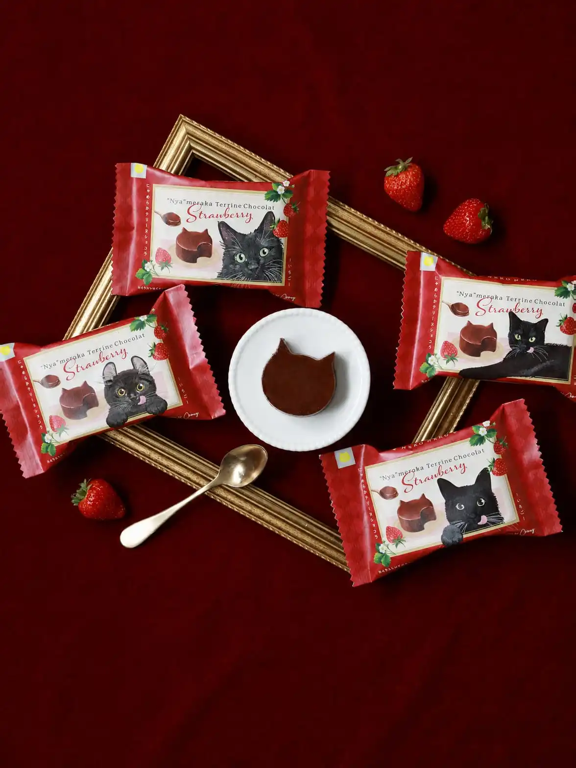 Cat-shaped chocolate strawberry terrine next to its red wrappers on deep red satin