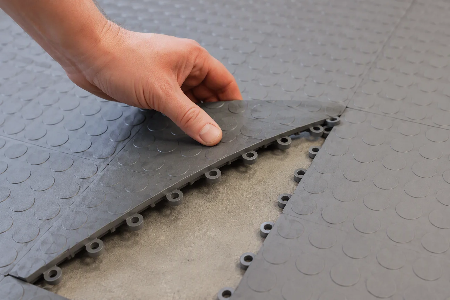 Lifting a single interlocking garage floor tile to reveal the click connectors