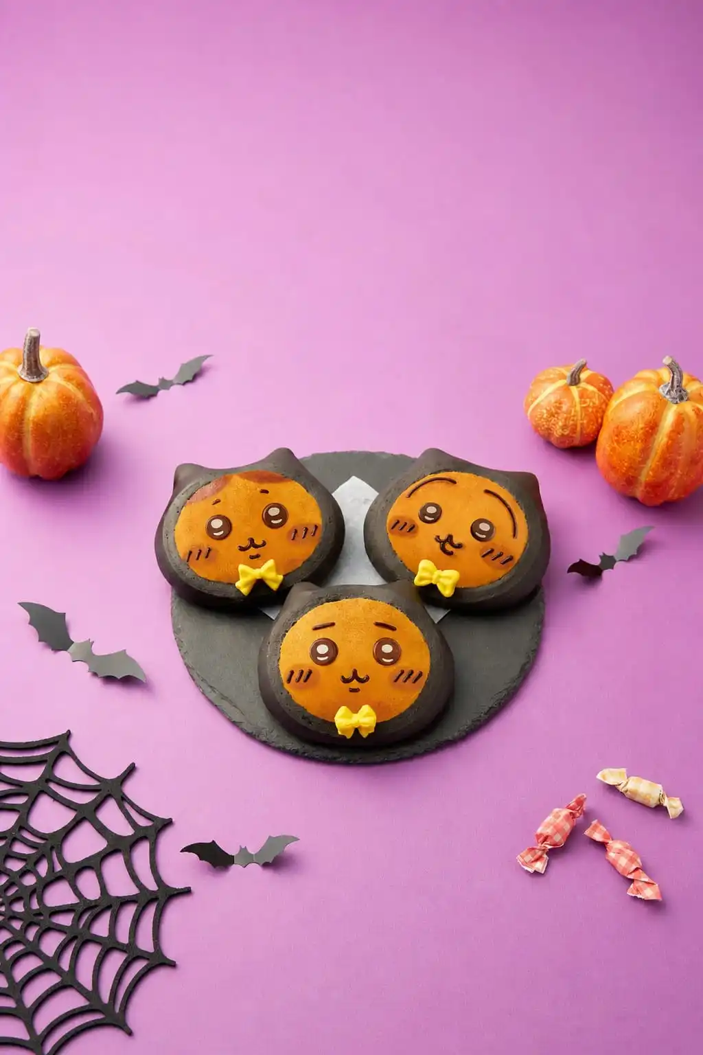 Three Chiikawa Bakery black-cat Halloween breads with orange faces and yellow bow ties on a slate plate