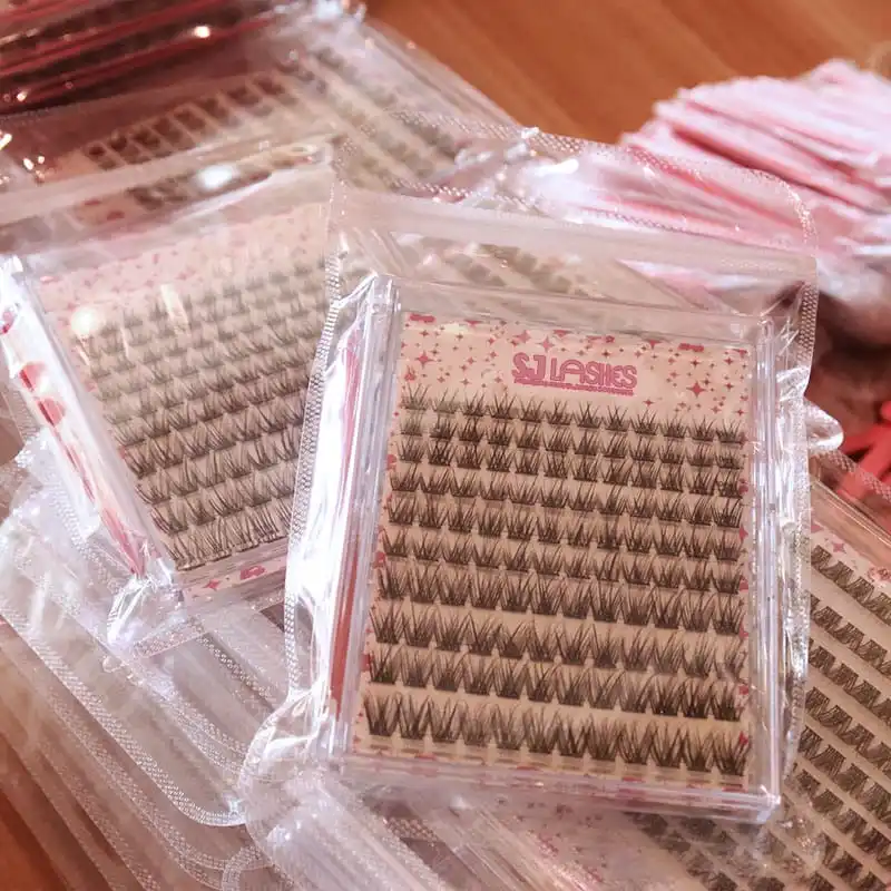 Bulk packed printed lash cards in clear zip bags, stacked in a carton with cards visible through the bags and pink lash segment fans showing - cluster lash card wholesale