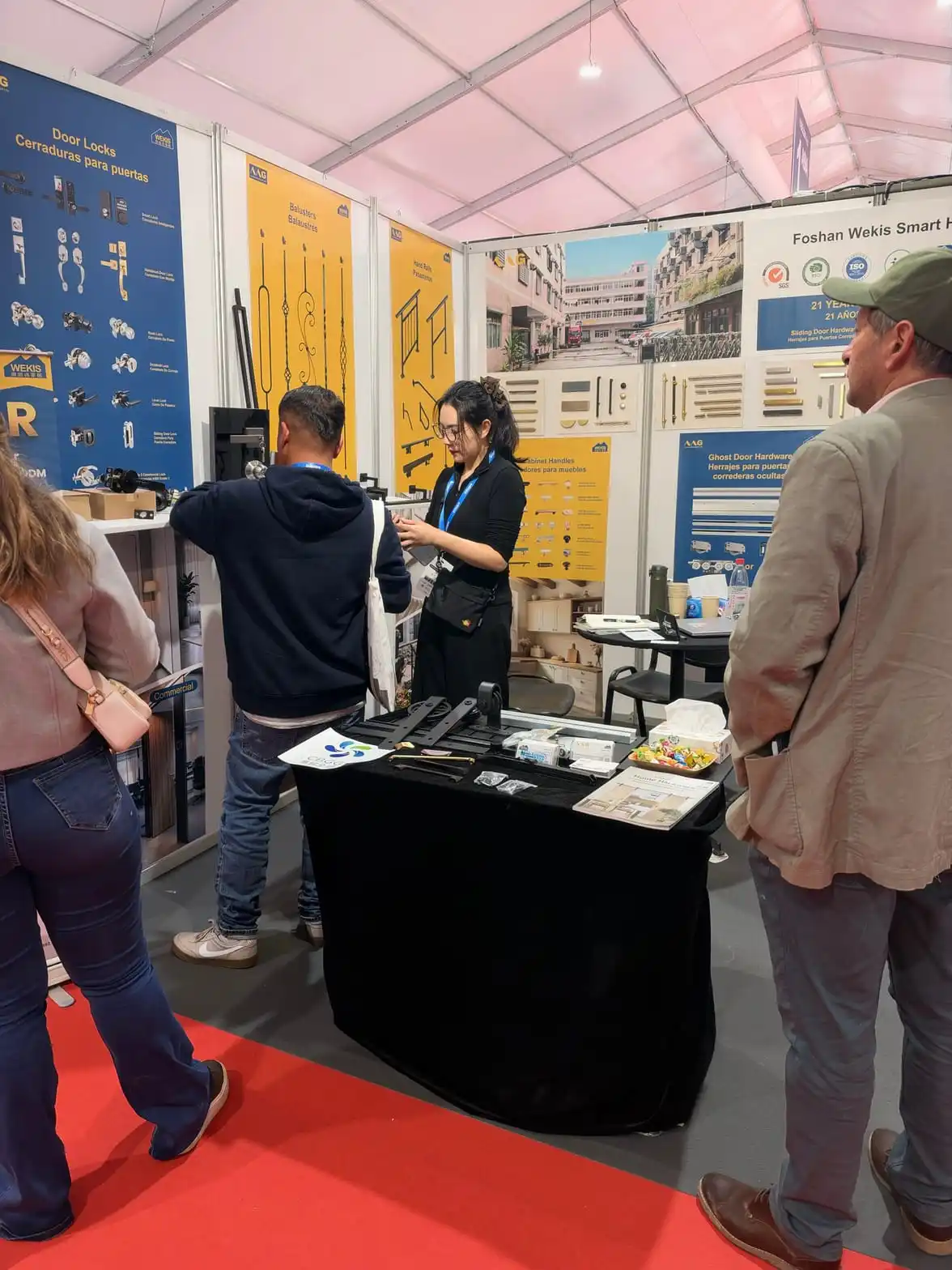 Un membre de l'équipe Wekis présente le panneau mural de poignées de meubles à un visiteur sur le stand EDIFICA 2026.