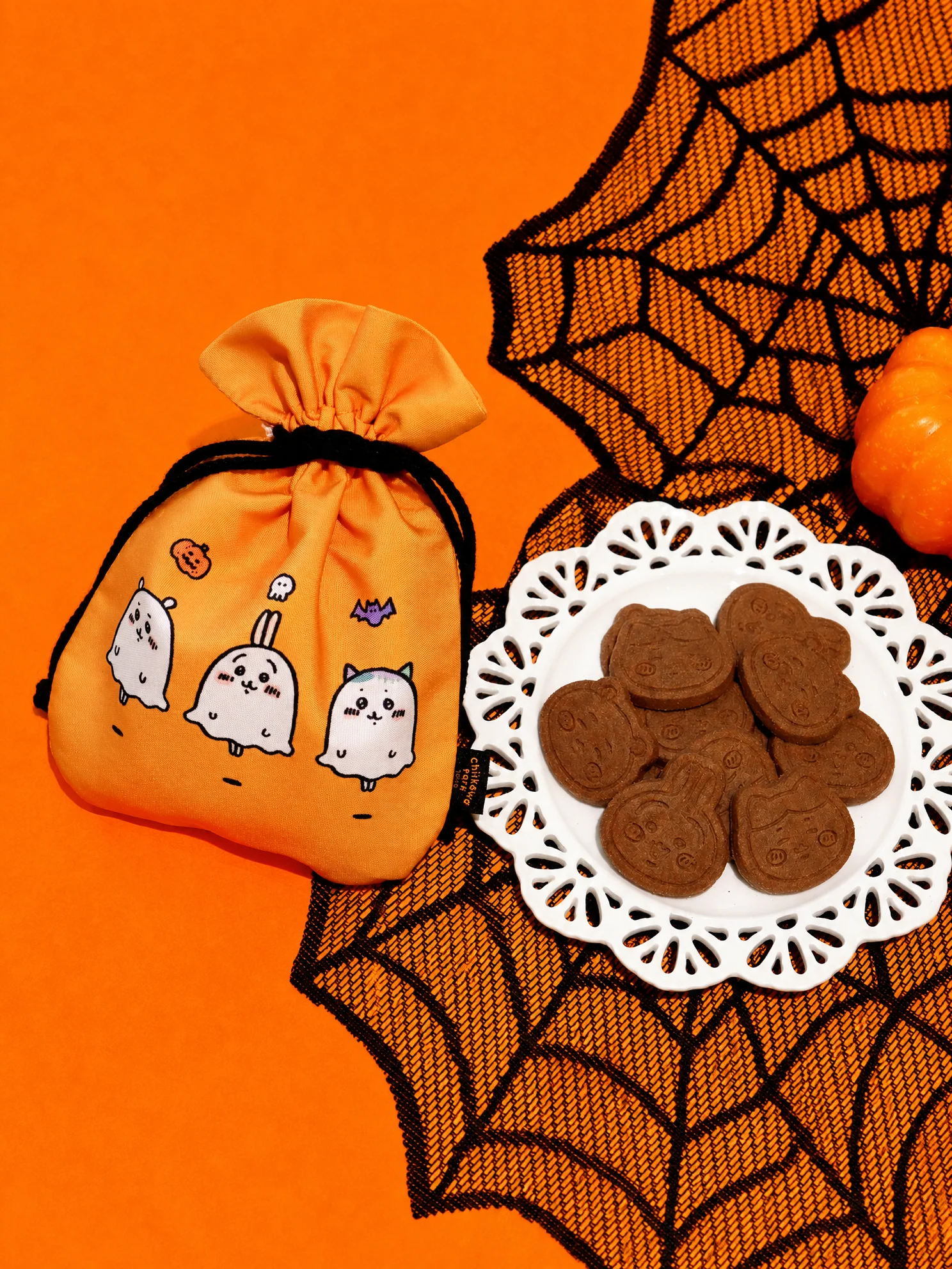 Chiikawa Park Halloween drawstring-bag cookies in an orange ghost-print pouch with cocoa cookies on a lace plate