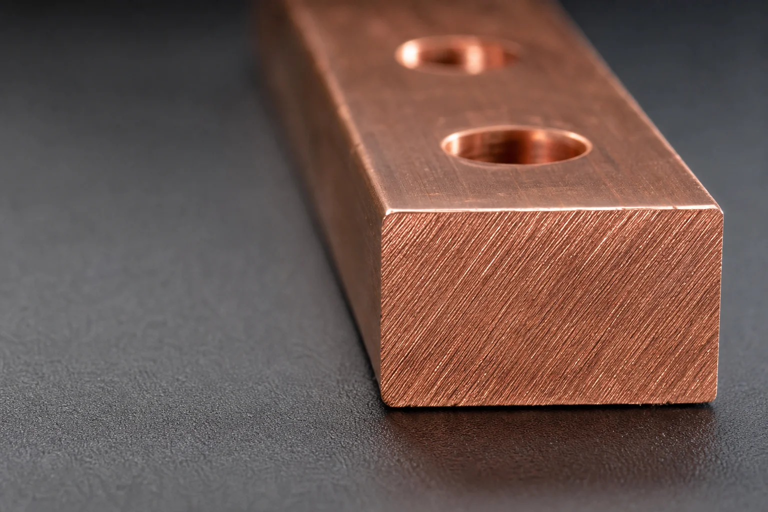Vista macro del extremo cortado de una barra colectora de cobre que muestra la sección rectangular y los taladros