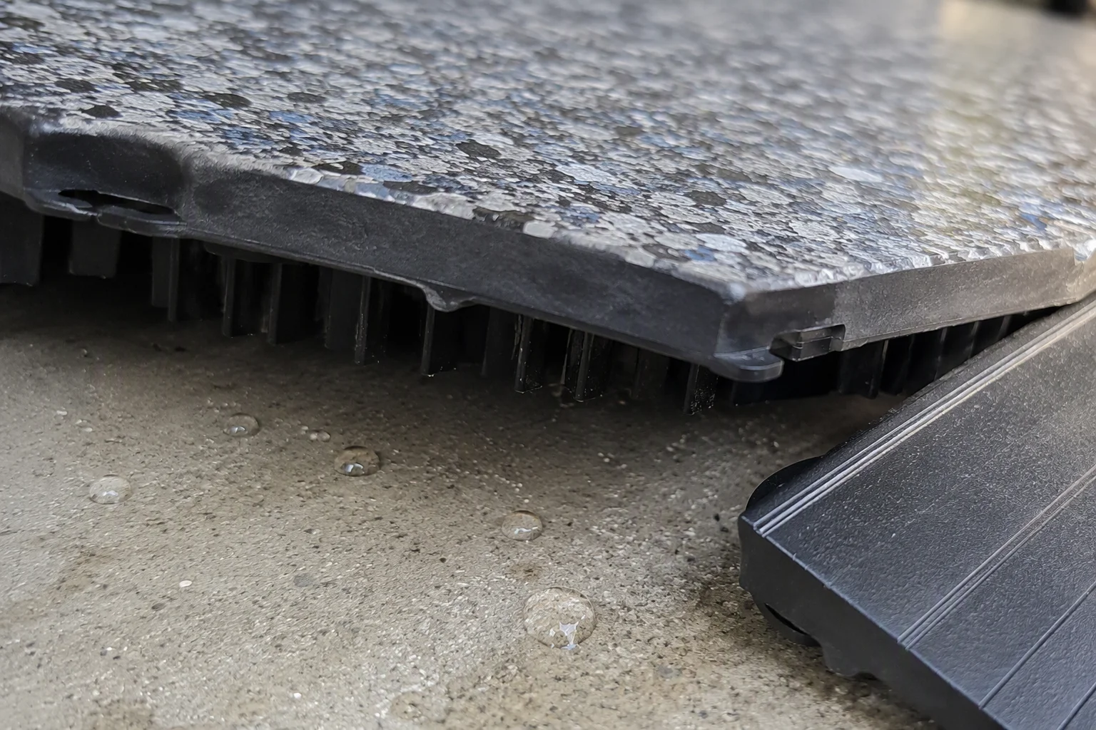 Air gap under a lifted interlocking garage floor tile above a damp concrete slab