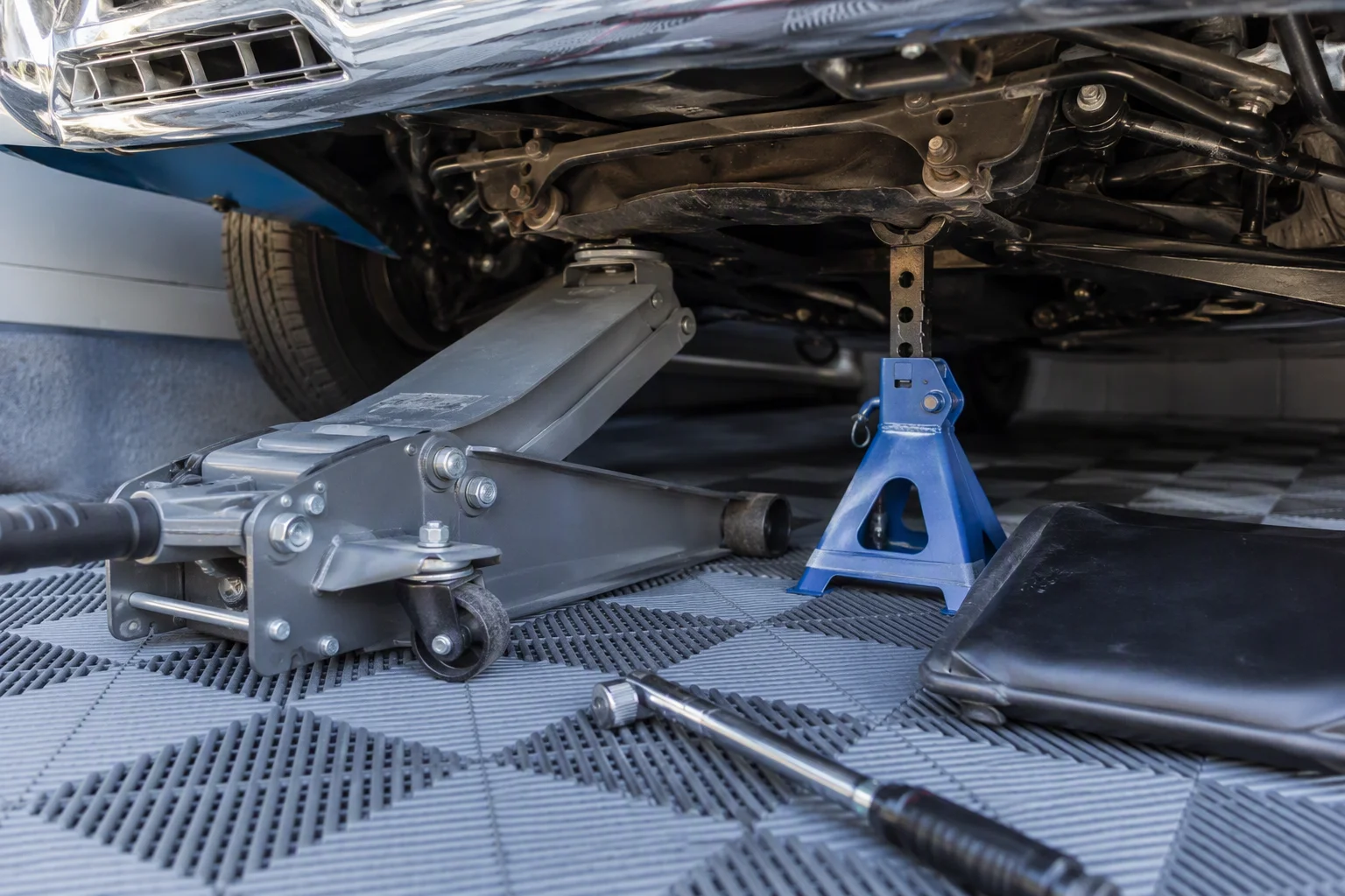 Trolley jack and jack stand under a classic car on interlocking garage floor tiles