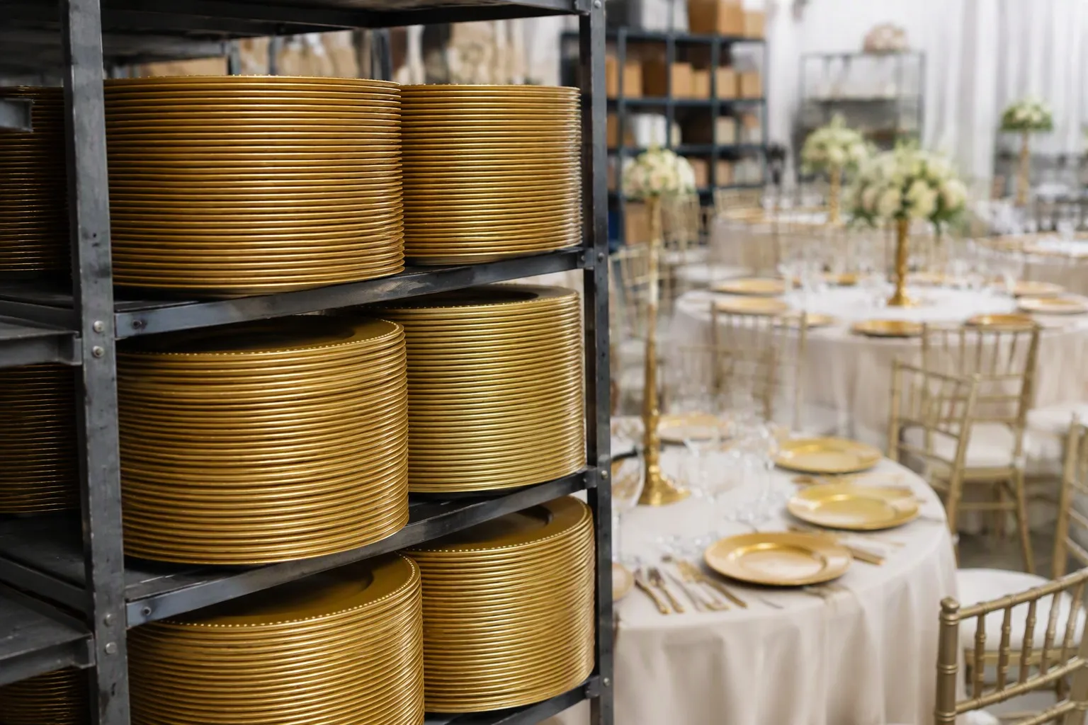 Large stack of gold charger plates in an event rental inventory with elegant tables in the background