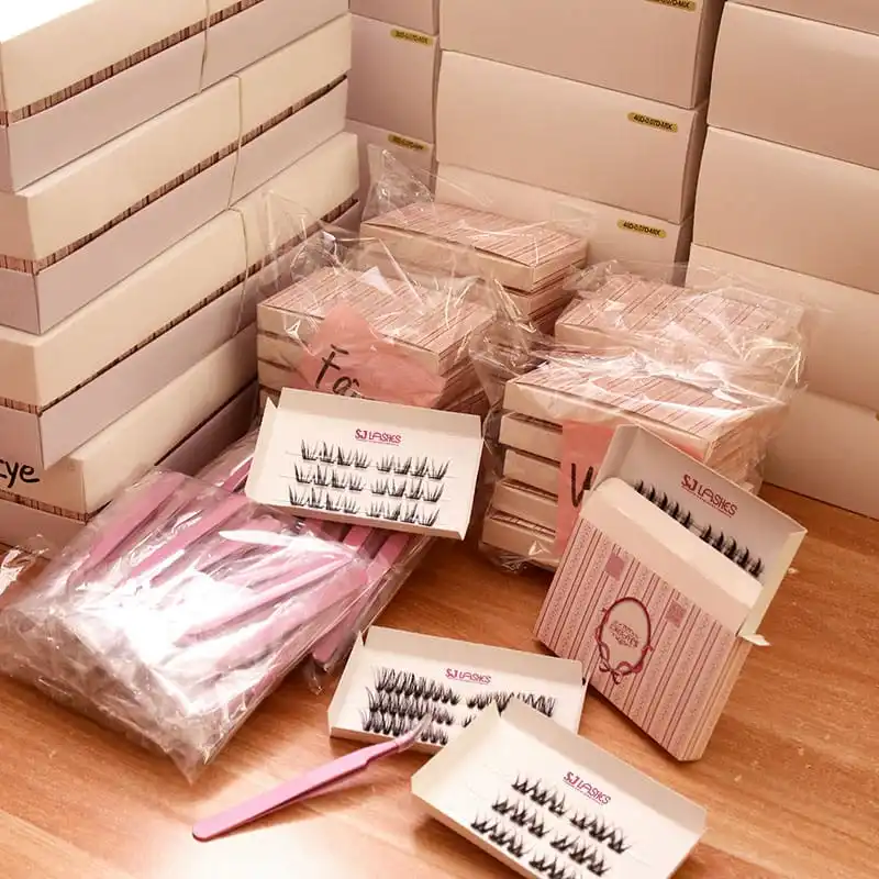 Cream and pink lash boxes stacked in bulk during packing, open boxes showing white printed lash cards, pink tweezers in bags and pink card sleeves - lash packaging bulk production