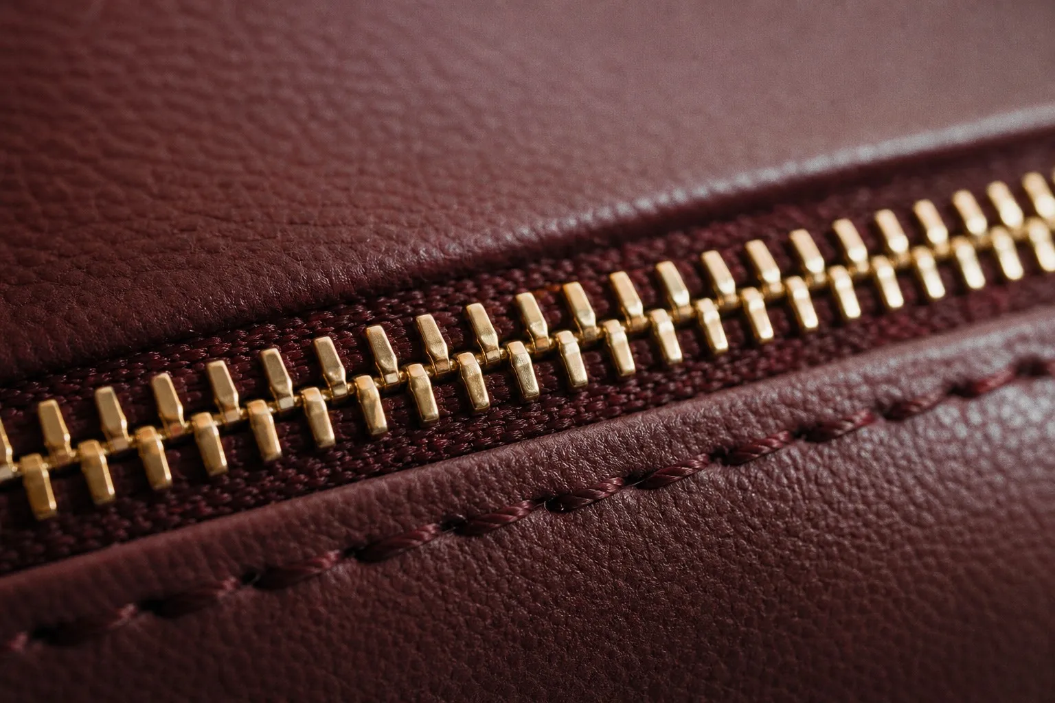 Macro close-up of a gold zipper and stitching on a burgundy leather cosmetic bag