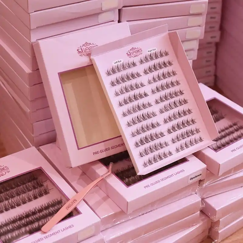 Stacked pale pink pre-glued segment lash boxes in bulk on a pallet with a pink SJ LASHES branded applicator tweezer in the foreground - segment lash box bulk production