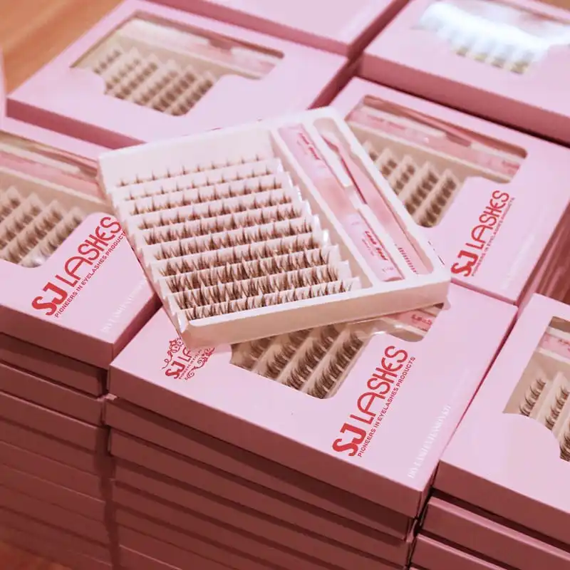 Stacks of pink DIY lash extension kit boxes in bulk with one open box showing the white molded tray of lash clusters and the bond seal and tool in their channels - lash kit boxes in bulk