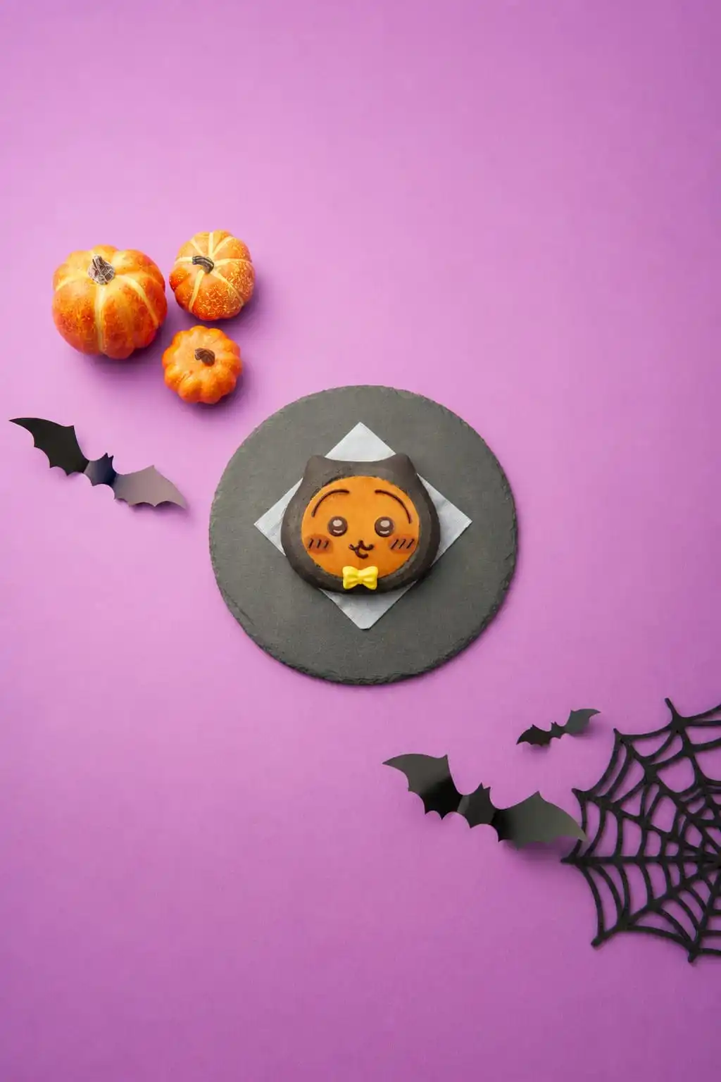A black-cat Halloween bread with a Hachiware-style face on a slate plate with pumpkins and bat decorations