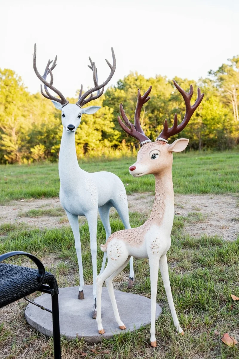 An outdoor deer statue wearing a knitted sweater with Christmas lights wrapped around its antlers during winter.