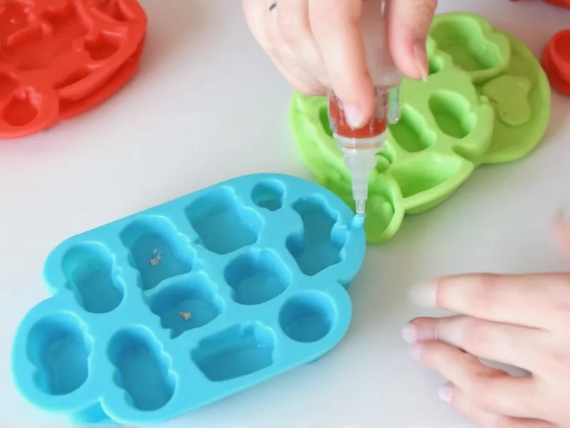 Pouring gummy mixture into silicone bear molds with squeeze bottle