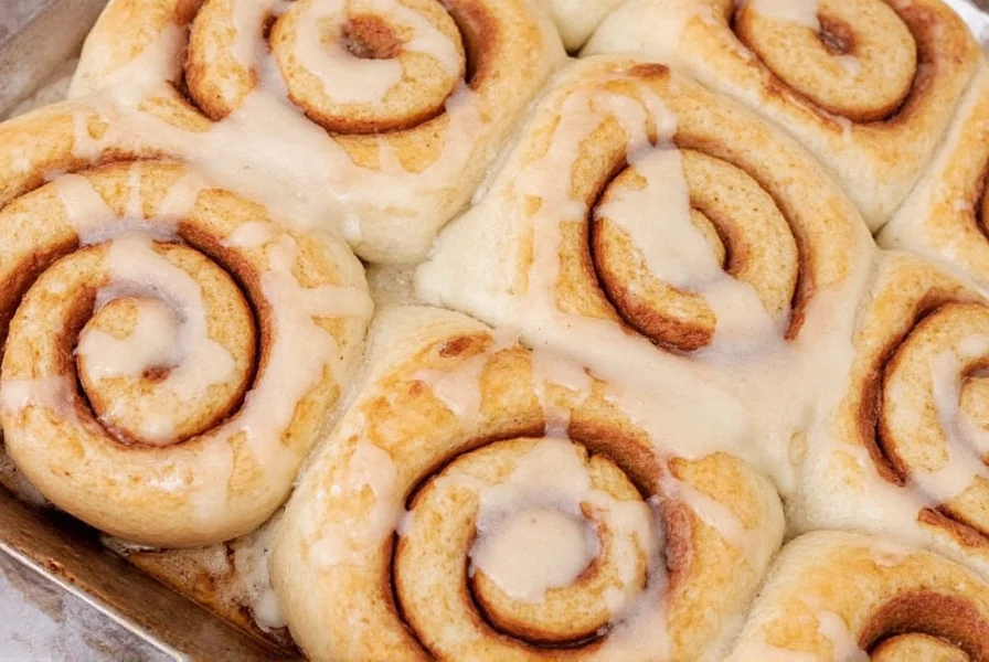 Professional baker hand-rolling cinnamon roll dough with perfect spiral pattern showing even cinnamon distribution