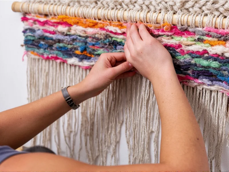Hands weaving recycled fabric strips into wall art