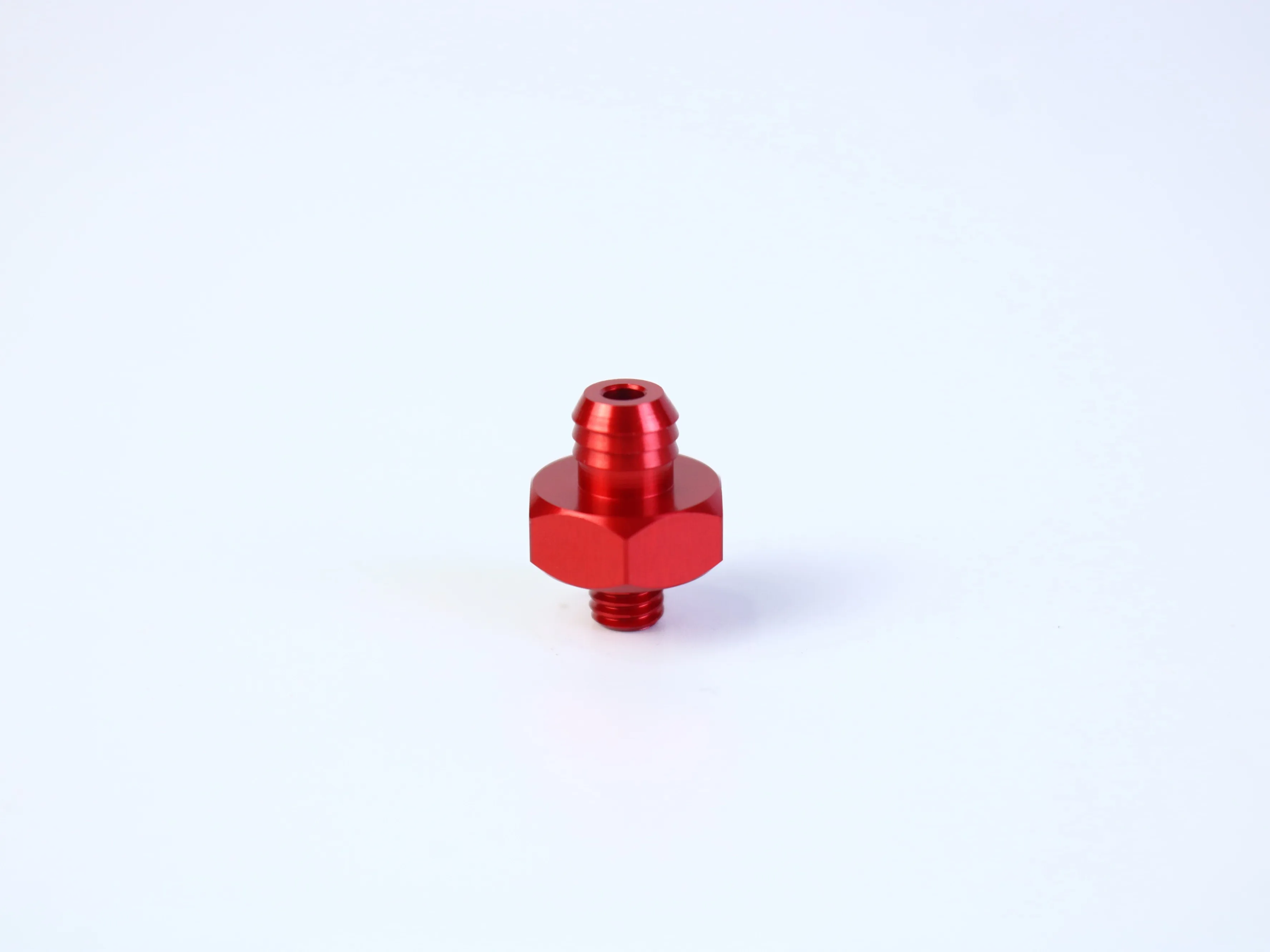 Red CNC turned threaded fitting with a hexagonal wrench section and central opening