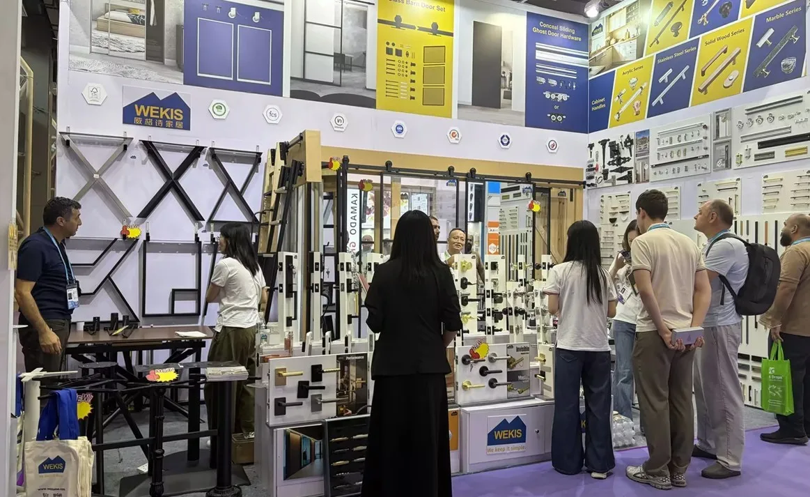 Des visiteurs explorent le mur de produits du stand Wekis à la Foire de Canton, accompagnés d'un membre de l'équipe qui passe devant l'exposition.