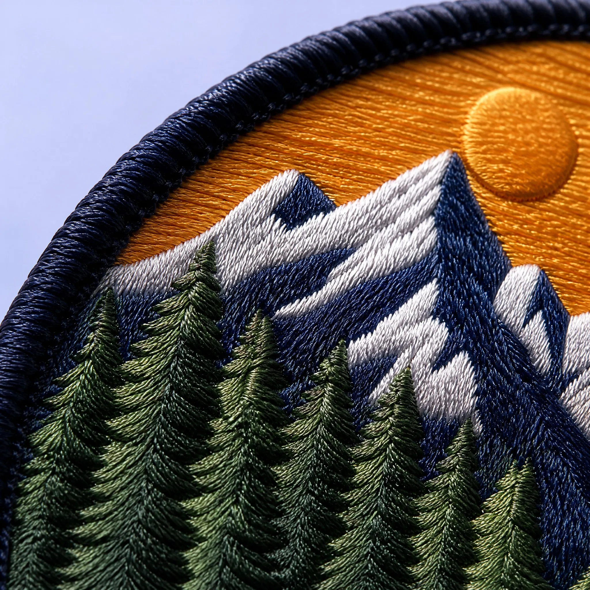 4K Macro Close-up of Mountain Landscape Embroidered Patch showing High Thread Density on Alpine Peak, Golden Sun, and Pine Tree Needles