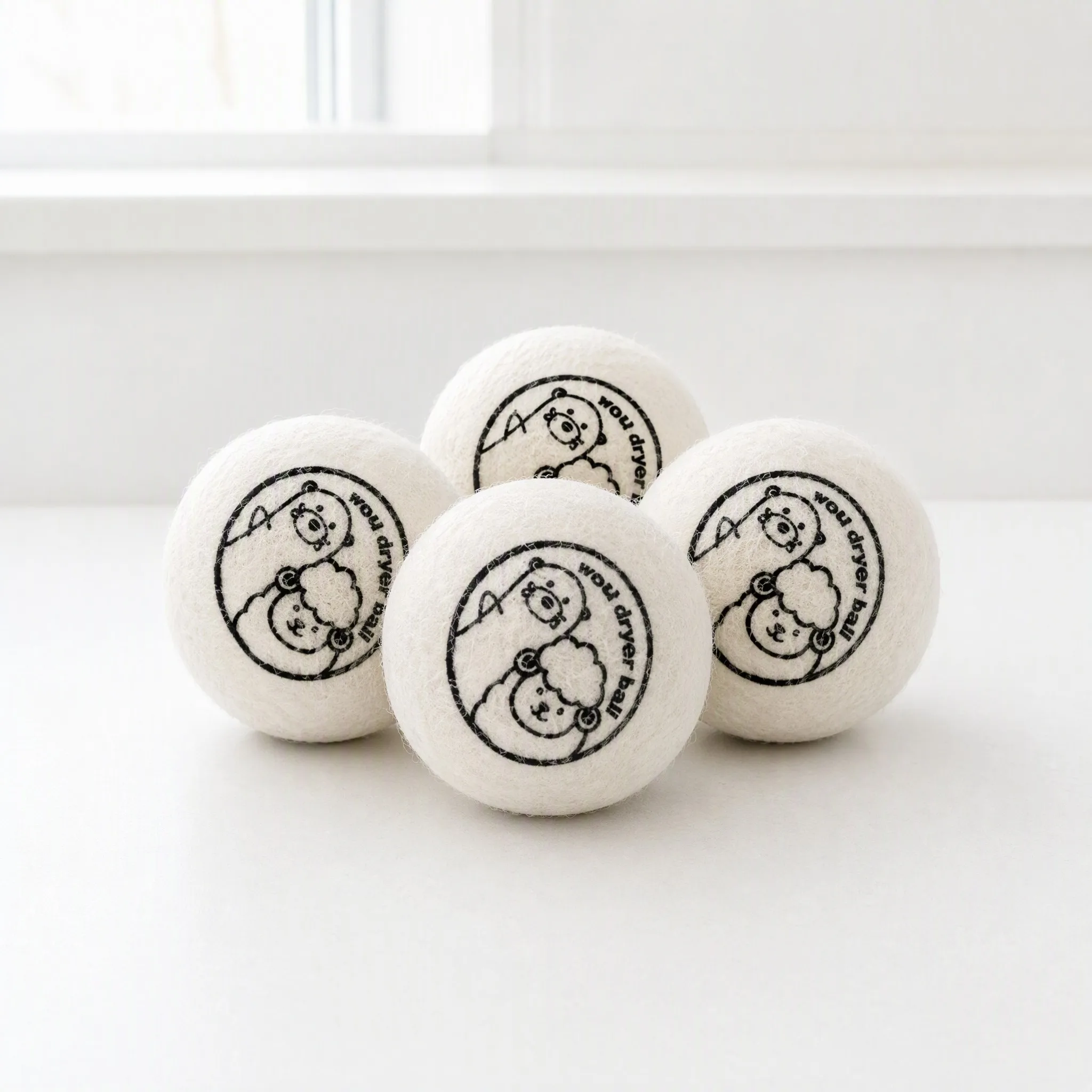 Wool dryer balls printed with a circular badge logo stamp styled in a white wire basket with a plant