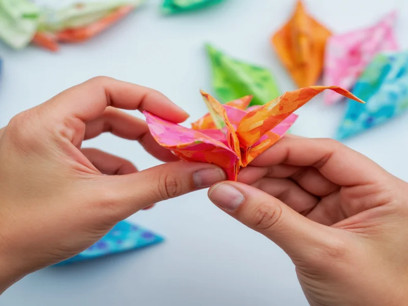 Hands folding colorful origami crane with recycled paper