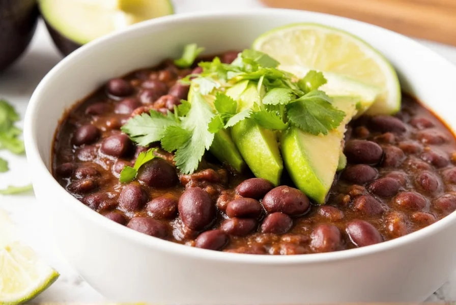 Finished black bean chili served in a white bowl with avocado slices, cilantro, and lime wedges as toppings