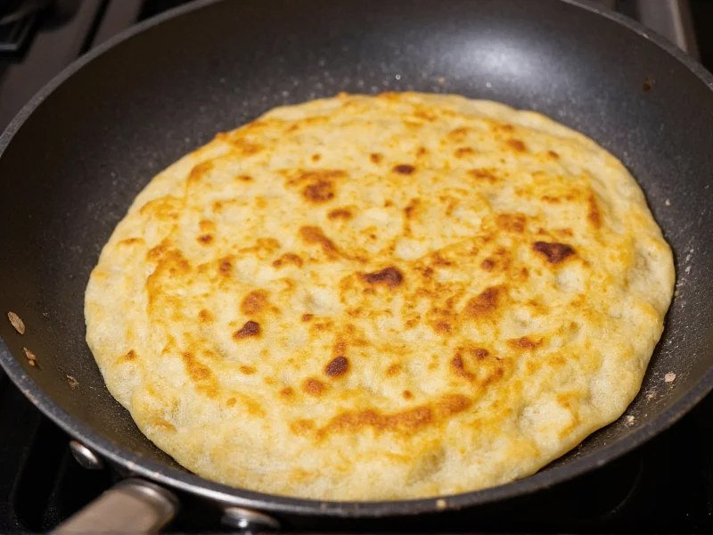 Tortilla cooking in skillet showing perfect golden spots and puff