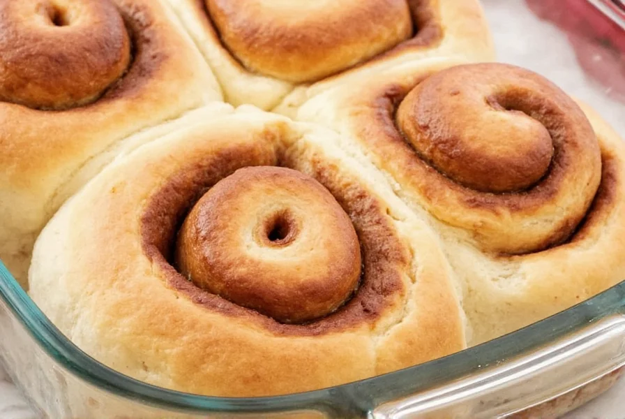 Perfectly golden homemade cinnamon buns with cream cheese glaze dripping between layers on a white ceramic plate