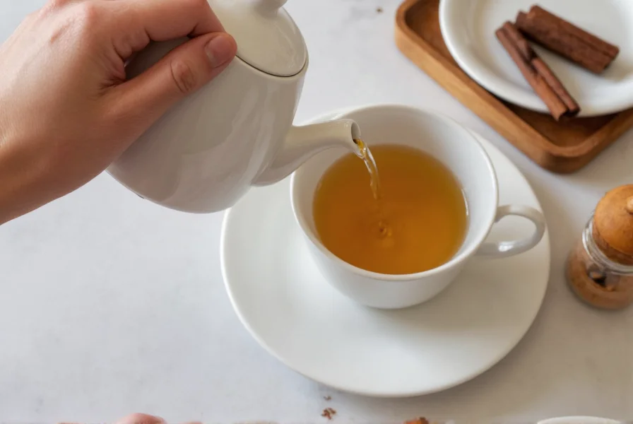 Hand pouring golden cinnamon tea from a ceramic teapot into a white mug