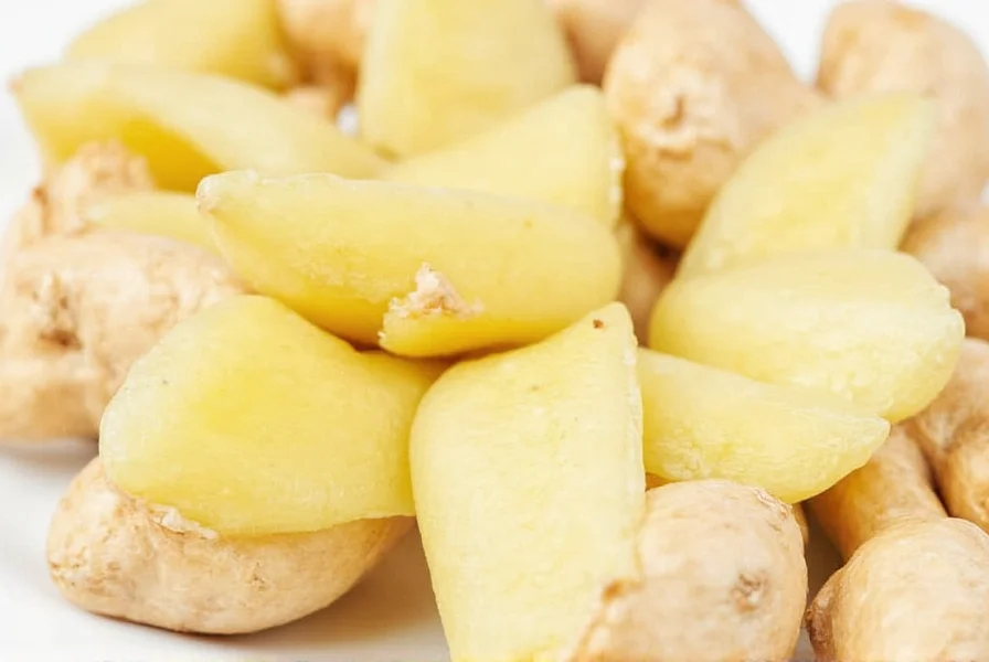 Close-up of hand using metal spoon to peel ginger root on cutting board